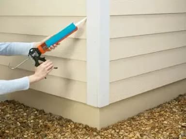 Person using a caulking gun on home siding