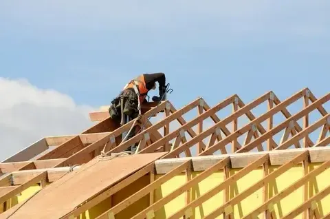 Construction worker installing roof framework on a building.