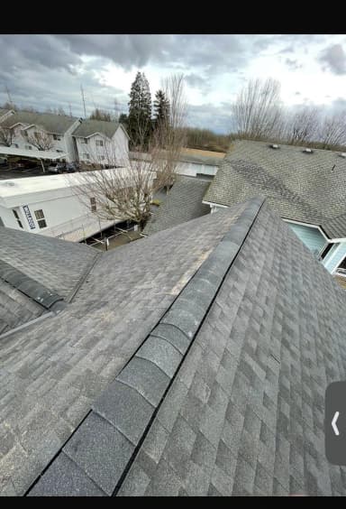 Top view of a residential roof with shingles and cloudy sky.