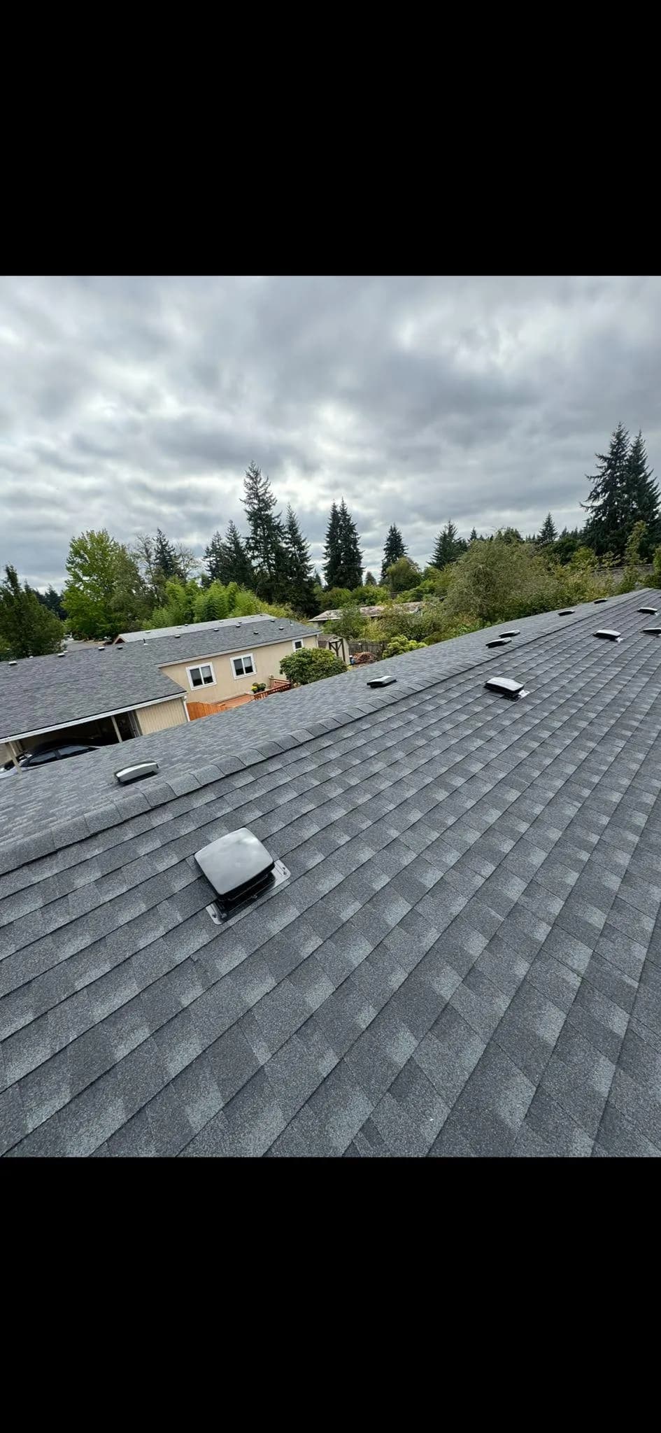 Aerial view of a gray shingle roof with skylights in a residential area.