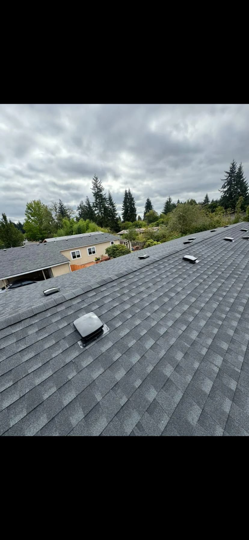 Aerial view of a gray shingle roof with skylights in a residential area.