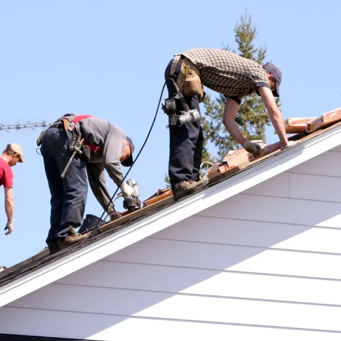 Three workers roofing a house under clear blue skies
