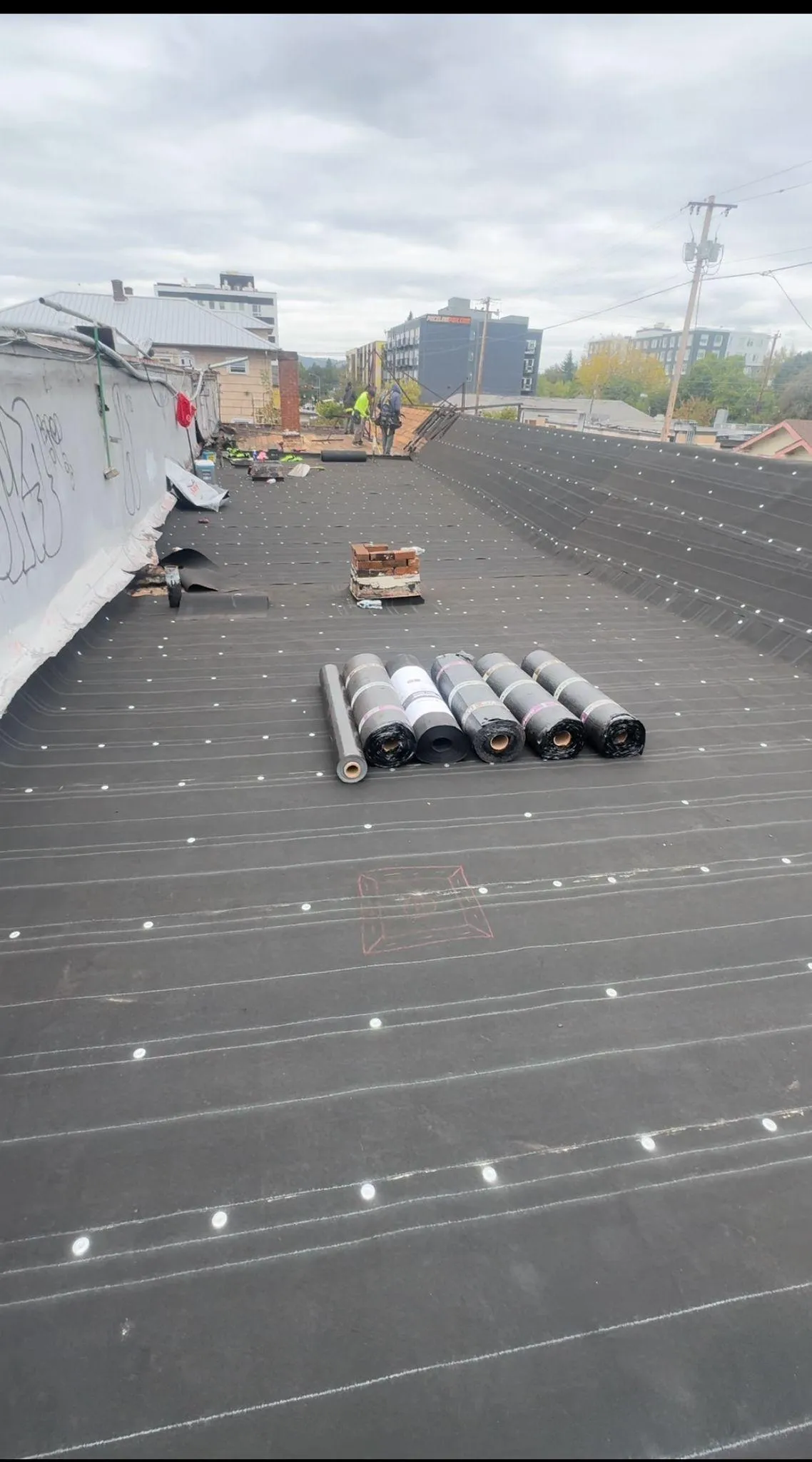 Flat roof construction with rolled materials and workers