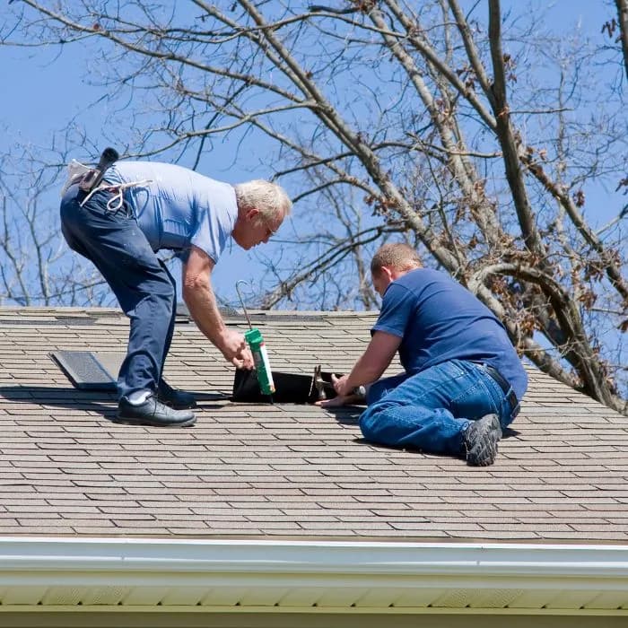 Two men repairing a roof under a clear blue sky.