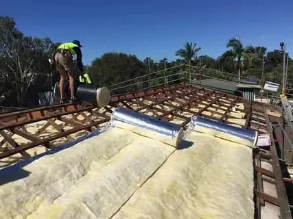 Worker installing insulation on roof with bright blue sky